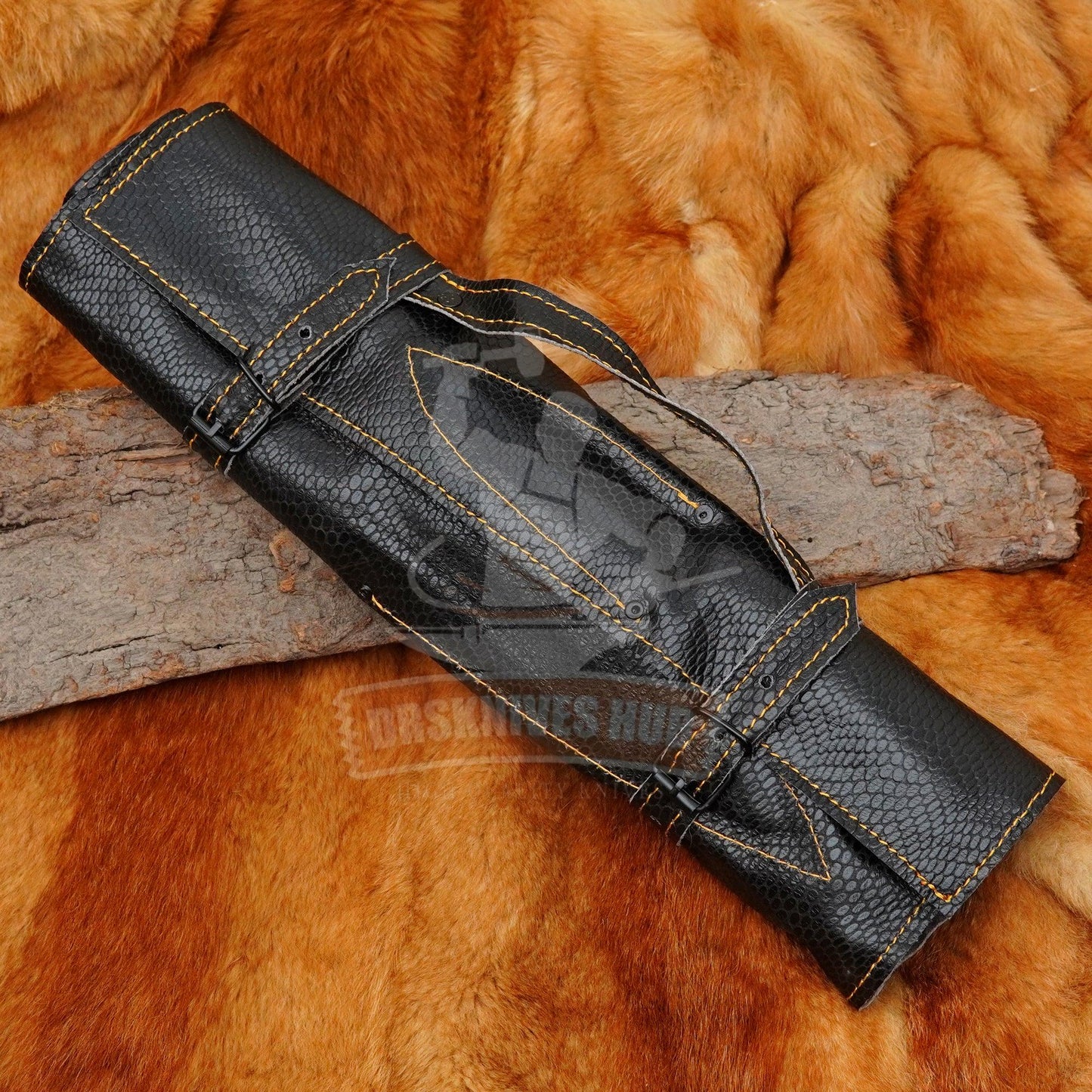 Black textured knife roll with yellow stitching on rustic wood and fur background