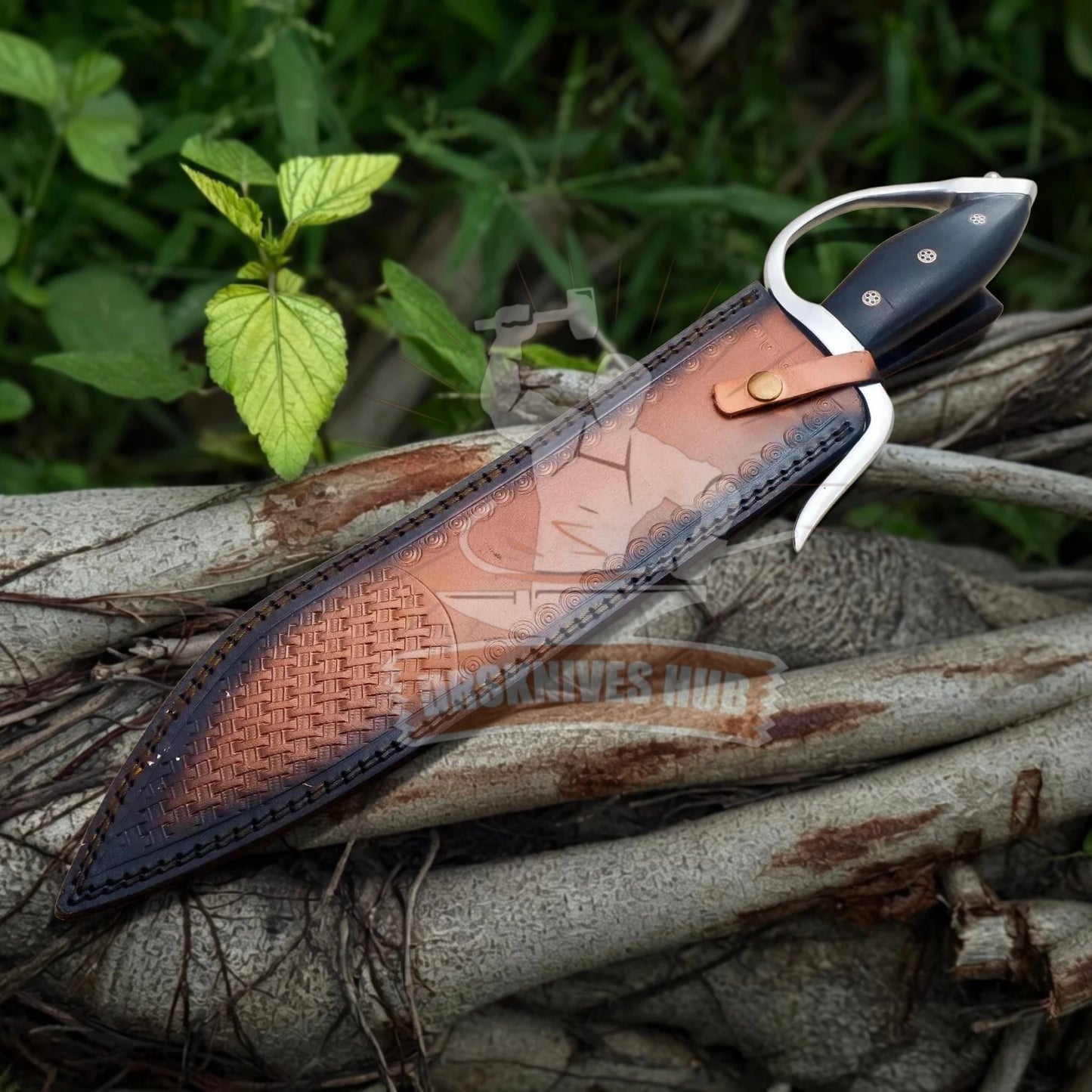 A fixed-blade knife with a black handle and silver guard, shown partially sheathed in a brown woven leather sheath, resting on tree roots outdoors with green foliage in the background.